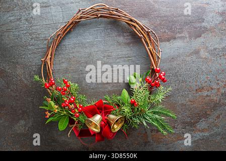 Weihnachtskranz aus natürlichen Zweigen, rote stechpalmenbeeren mit roter Schleife und goldener Glocke. Stockfoto