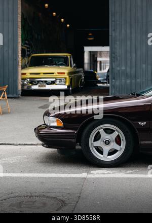 Klassische amerikanische Autos auf der Straße. Vorderteil des dunkelburgunderfarbenen Chevrolet Impala der 1990er Jahre im Vordergrund, hellgelber GMC Pickup Truck der 1960er Jahre Stockfoto