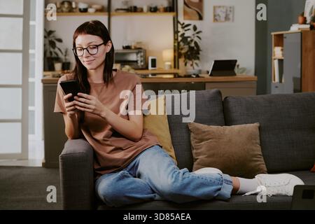 Junge kaukasische Frau, die auf dem Sofa sitzt und das Smartphone zum Online-Shopping benutzt Stockfoto