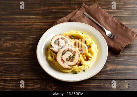 Schweinebraten mit Pilzen, Käse, getrockneten Tomaten in Soße serviert mit Kartoffelpüree auf einer hellen Platte auf braunem Holztisch Stockfoto