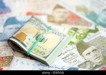 Ein Haufen US-Dollar-Scheine liegt auf einer großen Menge pakistanischer Rupien-Banknoten aus nächster Nähe. Amerikanisches Geld lügt auf Pakistans Geldrechnungen. Das Konzept der Ökonomie und des Devisenaustausches in Pakistan Stockfoto