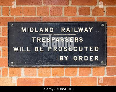 Ein altes gusseisernes Warnschild an einer Ziegelmauer, das erklärt, dass Eindringlinge auf dem Grundstück der Midland Railway per Beschluss verfolgt werden Stockfoto