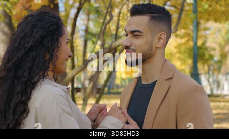 Hispanisches glückliches Paar spricht unbeschwert im Herbstpark multiethnische Familie kaukasische Frau spricht mit arabischem Mann in Stockfoto