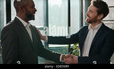 Zwei lächelnde freundliche, vielseitige Geschäftsleute, ein erfolgreiches Handschütteln Männer im Büro Kaukasischer Mann, der die Glückwünsche unterstützt Stockfoto
