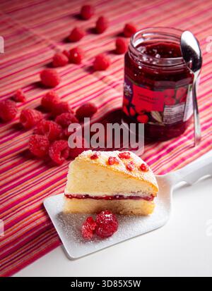 Ein Victoria Sponge Cake, Himbeeren, die neben dem Kuchen auf einem Keramikspachtel platziert werden Stockfoto