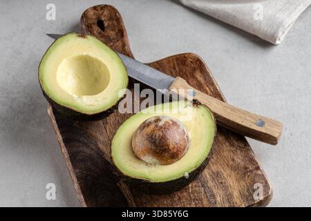 Frische Avocado auf einem hölzernen Schneidebrett mit Messer und Serviette auf grauem Hintergrund. Gesunde exotische Früchte. Super Essen. Stockfoto