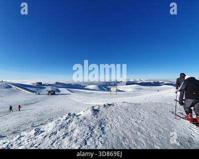 Skifahrer auf einem hellen, schneebedeckten Berghang unter einem klaren blauen Himmel. Stockfoto