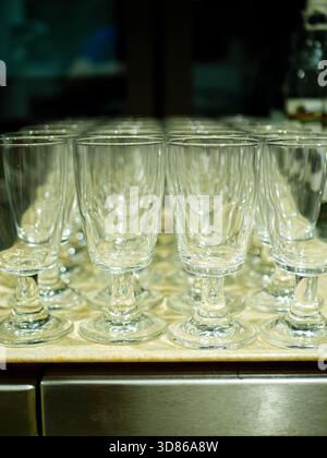 Reihe sauberer, leerer Weingläser auf einer Metalltheke im Inneren der Restaurantküche, bereit für den Service und professionelles Catering im kommerziellen Bereich Stockfoto