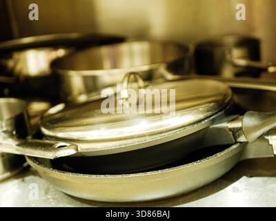 Nahaufnahme von Edelstahlpfannen mit Deckeln, die auf Küchenregalen im Arbeitsbereich eines gewerblichen Restaurants gelagert werden. Hochwertiges Foto Töpfe aus Edelstahl, Stockfoto