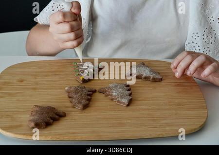 Kinderhände schmücken Lebkuchenkekse mit Puderzucker auf einem Holzbrett. Stockfoto