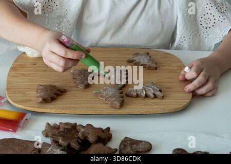 Kinderhände schmücken Lebkuchenkekse mit Puderzucker auf einem Holzbrett. Stockfoto