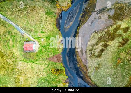 Blick aus der Vogelperspektive auf ein einsames Haus mit einem roten Dach, eingebettet in die lebhafte grüne Landschaft entlang des geflochtenen Flusses Hvíta, Fluss Hvíta, Island. Stockfoto