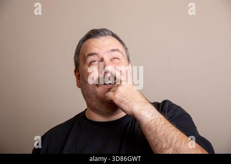 Ein Mann mit Bart und Schnurrbart macht ein komisches Gesicht und zeigt mit dem Finger. Er trägt ein schwarzes Hemd und ist in verspielter Stimmung Stockfoto