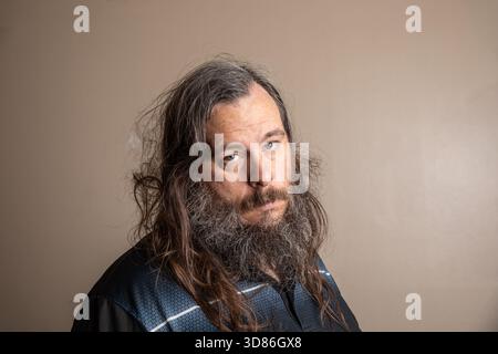 Ein Mann mit Bart und langen Haaren sitzt vor einer Wand Stockfoto