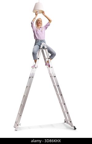 Frau, die auf einer Leiter sitzt und eine Glühlampe auf einer Pendelleuchte auf weißem Hintergrund platziert Stockfoto