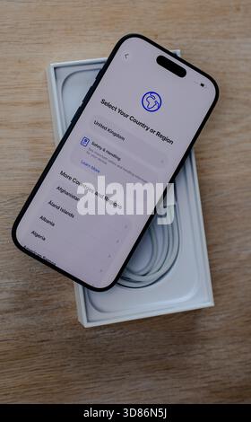 Smartphone mit Bildschirm zur Länderauswahl auf der offenen Box mit USB-C-Kabel auf Holzoberfläche Stockfoto