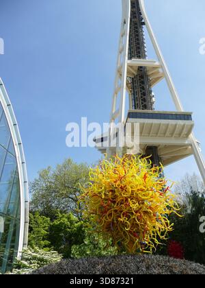 SEATTLE - 25. APR 2025 - Moderne gelbe und rote Glasskulptur von Dale Chihuly, die in einem Garten mit der Space Needle im Hintergrund aufragt Stockfoto