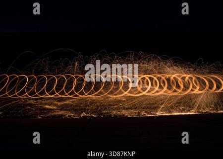 Langzeitaufnahme von kreisförmigen Lichtbahnen und Funken von sich bewegenden Lichtquellen vor dunklem Hintergrund. Stockfoto