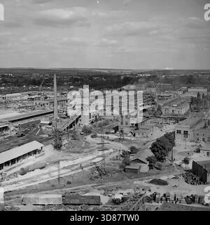 Slawjansk, Ukraine, UdSSR - 1970er Jahre: Panoramablick auf das Armature-Isolator-Werk AIZ. Ein hoher gemauerter Schornstein, Produktionswerkstätten und Fördergalerien dominieren die Landschaft. Eisenbahngleise mit Güterwagen und Materialstapeln bedecken den Vordergrund. Unter den Gebäuden befinden sich Hochspannungsmasten. Stadtviertel erstrecken sich bis zum Horizont. Dieses Schwarzweiß-Archivfoto zeigt die Großindustrie und die Infrastruktur der friedlichen Donbass-Stadt. Stockfoto