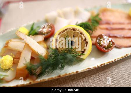 Auf einer wunderschön angeordneten Platte finden Sie eine Auswahl an Räucherfleisch, geschnittenem Gemüse und farbenfrohen Beilagen. Frische Zitrone und Kräuter sorgen für ein lebendiges T Stockfoto