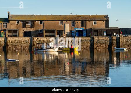 Malerischer Blick auf den Hafen in Lyme Regis während der goldenen Stunde, mit verankerten Booten und warmes Sonnenlicht reflektiert auf dem Wasser, Dorset, Großbritannien. Stockfoto