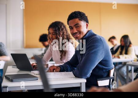 Porträt eines lächelnden Teenager-Schülers, der am Schreibtisch sitzt und Bücher im Klassenzimmer hat Stockfoto