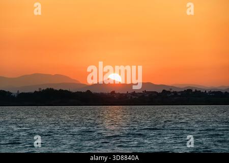 Der Sonnenuntergang oder -Aufgang hinter den Hügeln der Küste von Collioure, Frankreich, wirft ein intensives orangefarbenes Licht und bildet die historische Stadt Stockfoto