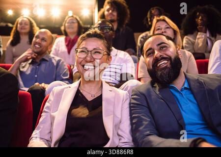 Lächelnde männliche und weibliche Freunde, die Bühnenspiele beobachten, während sie im beleuchteten Theater sitzen Stockfoto