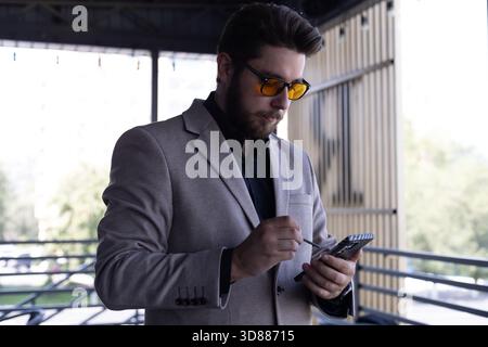 Ein Mann steht auf einem Balkon und schaut auf sein Handy Stockfoto