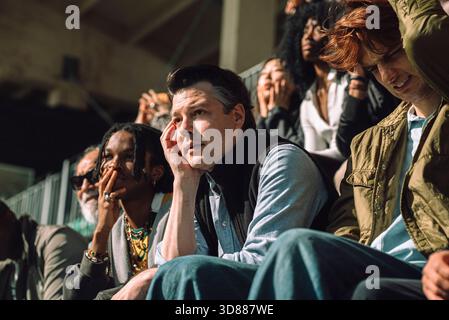 Trauriger männlicher Zuschauer sitzt ungläubig am Sportstadionstand an sonnigen Tagen Stockfoto
