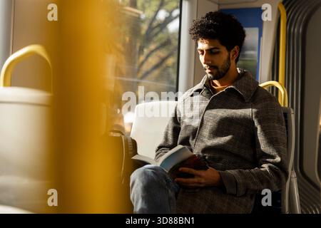 Mann liest Buch, während er an sonnigem Tag im Bus sitzt Stockfoto