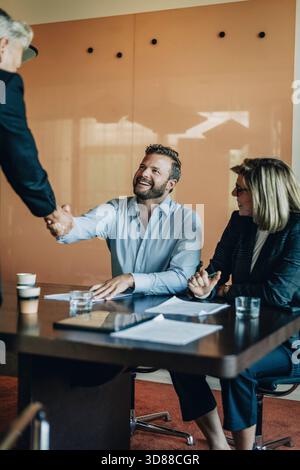 Glücklicher männlicher Jurist schüttelt nach Geschäftsvereinbarung im Amt Hand mit einem leitenden Kollegen Stockfoto