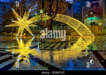 Beleuchtete Weihnachtssterninstallation reflektiert auf nassem Pflaster auf der Piazza Michele Muzii, vor Mercato Coperto Muzii in Pescara, Abruzzen, I Stockfoto