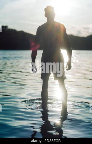 Sonnenlicht, das auf der Silhouettenaufnahme eines Mannes steht, der im Wasser des Sees steht Stockfoto