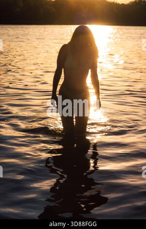 In der Silhouette einer Frau, die bei Sonnenaufgang im Wasser steht Stockfoto
