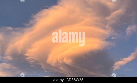 Die Schönheit einer einzigartigen Lentikularwolkenbildung vor blauem Himmel. Wolkenschichten werden bei Sonnenaufgang in W mit warmem Orange und Rosa beleuchtet Stockfoto