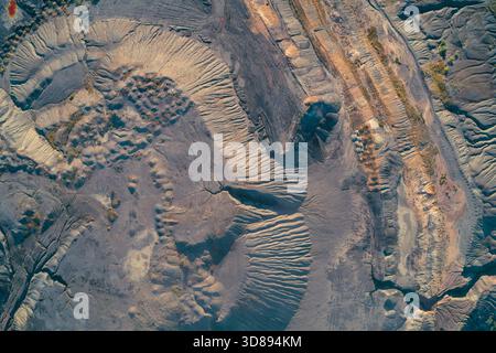 Top-Down-Drohnenaufnahme mit komplizierten Mustern von erodiertem Land, tiefen Schluchten und dunklem Industrieabfall. Schwere Umweltverheerungen und geologische Störungen durch den Bergbau Stockfoto