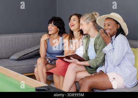 Verschiedene Gruppen von Frauen lachen zusammen auf der Couch und genießen die Freizeit drinnen. Vielfalt, Freundschaft, Zweisamkeit, Entspannung, Verbundenheit, Happiness || Model veröffentlicht Stockfoto