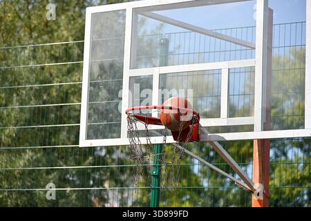 Nahaufnahme eines orangefarbenen Basketballballs in den Korb auf dem Platz im Freien, niedriger Winkel, Vorderansicht Stockfoto