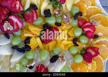Verschiedene geschnittene Früchte einschließlich Erdbeeren, Orangen, Trauben, Äpfel, Mango, Rosinen und Walnüsse Stockfoto