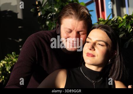 Ein Mann und eine Frau mittleren Alters teilen einen zarten Moment, in der Sonne gebadet, mit leuchtend grünen Pflanzen im Hintergrund, die eine ruhige und intime Umgebung schaffen Stockfoto
