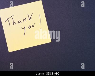 Dankeschön Haftnotiz auf dunklem Hintergrund – hellgelbe Haftnotiz mit „Danke!“ Nachricht in schwarzer Schrift auf dunklem texturiertem Hintergrund. Ideal für Stockfoto