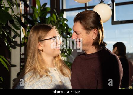 Ein Vater und eine Tochter genießen eine herzliche Interaktion, indem sie in einem sonnendurchfluteten, mit Grün geschmückten Raum ein Lächeln austauschen, was ihre enge Bindung und Zuneigung unterstreicht Stockfoto