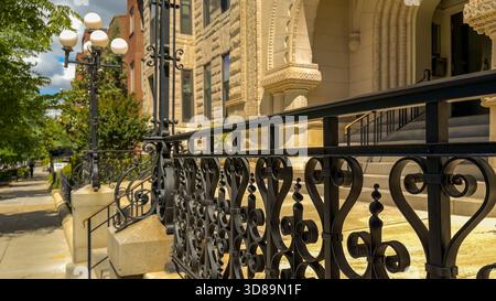 Dekorative schmiedeeiserne Geländer und Vintage-Lampenpfosten säumen den Eingang eines historischen Steingebäudes in einer ruhigen Stadtstraße. Stockfoto