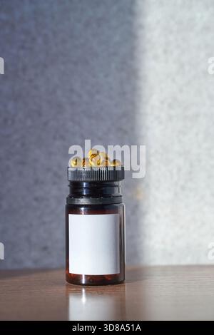 Bernsteinfarbene Kapselflasche auf Holzoberfläche mit Schattenspiel vor grauem, strukturiertem Hintergrund. Stockfoto