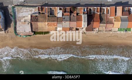 Blick über der Drohne auf zerstörte und farbenfrohe Fischerhäuser am Meer in Guardamar Stockfoto