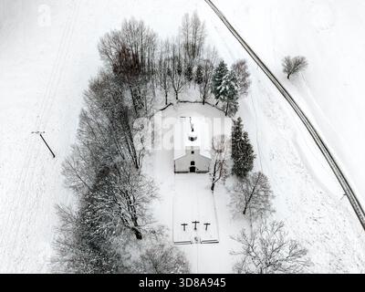 Drohnenblick auf die Calvary Kapelle in Ruzomberok mit schneebedeckten Bäumen und weißen Feldern um sie herum. Eine ruhige Winterlandschaft zeigt die Exaltatio-Kirche Stockfoto