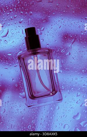 Auf dem Glas liegt eine Flasche Parfüm in Tropfen Wasser und Spritzern. Violettes Bokeh. Hinter Glasparfümflaschen Stockfoto