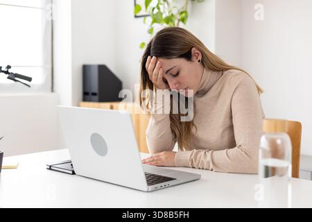 Junge Erwachsene Geschäftsfrau, die sich am Schreibtisch gestresst fühlt Stockfoto