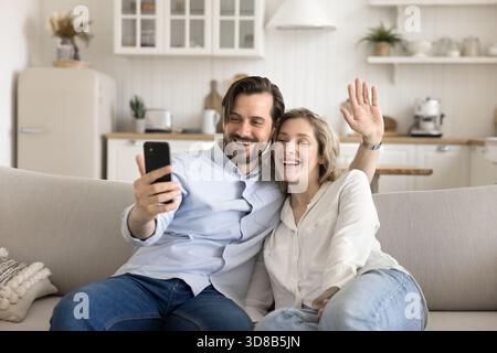 Glückliches Paar, das auf der Couch sitzt und mit Freunden per Video kommuniziert Stockfoto